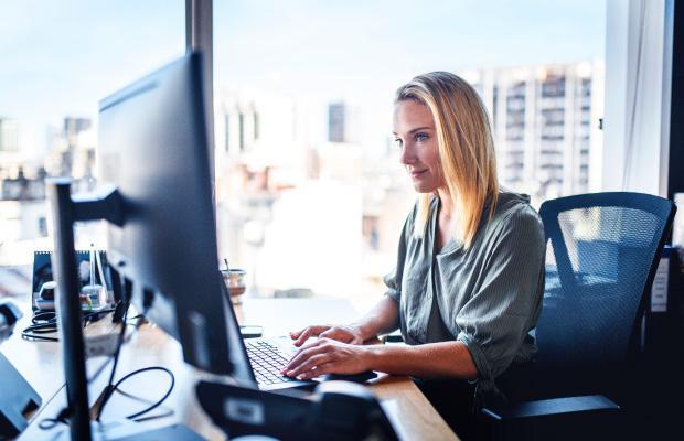 a blond woman sitting in an office in front of a monitor